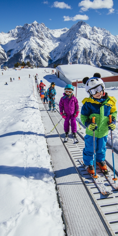 Kinder mit Skiern auf Förderband im Skigebiet Scuol