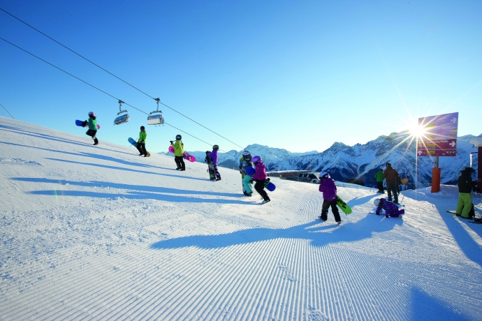 Kinder tragen Snowboards über Piste bei Scuol